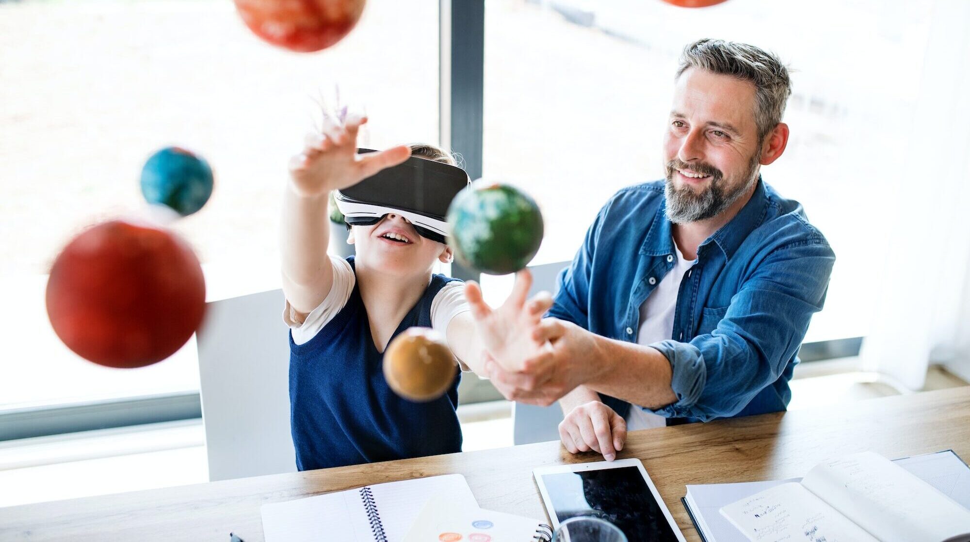 Mature father with small son and VR goggles indoors, working on school project